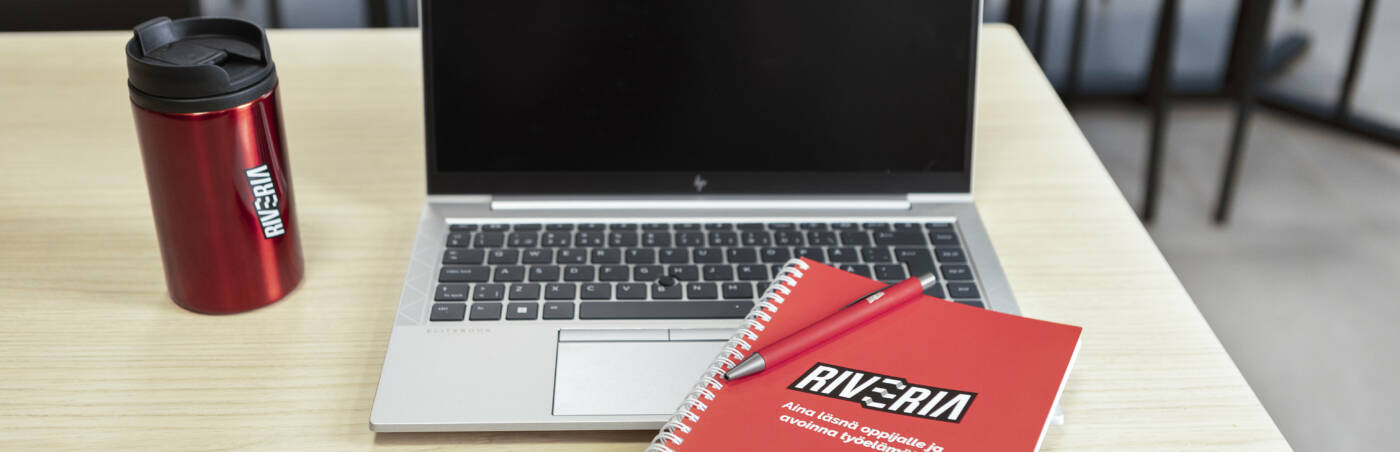 A laptop computer next to a thermos and a notebook with the Riveria logo.